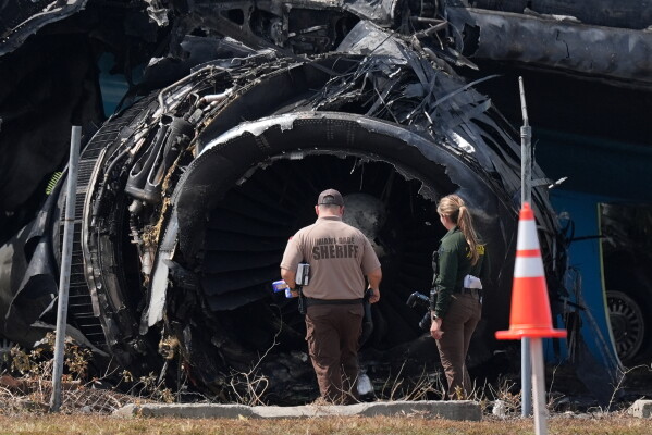 Law enforcement officers walk in front of a destroyed engine as they inspect an Amazon cargo plane two days after it overshot a runway at Miami International Airport, Tuesday, Sept. 8, 2026, in Miami. (AP Photo/Rebecca Blackwell)
