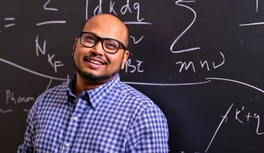A man with glasses smiles in front of a chalkboard