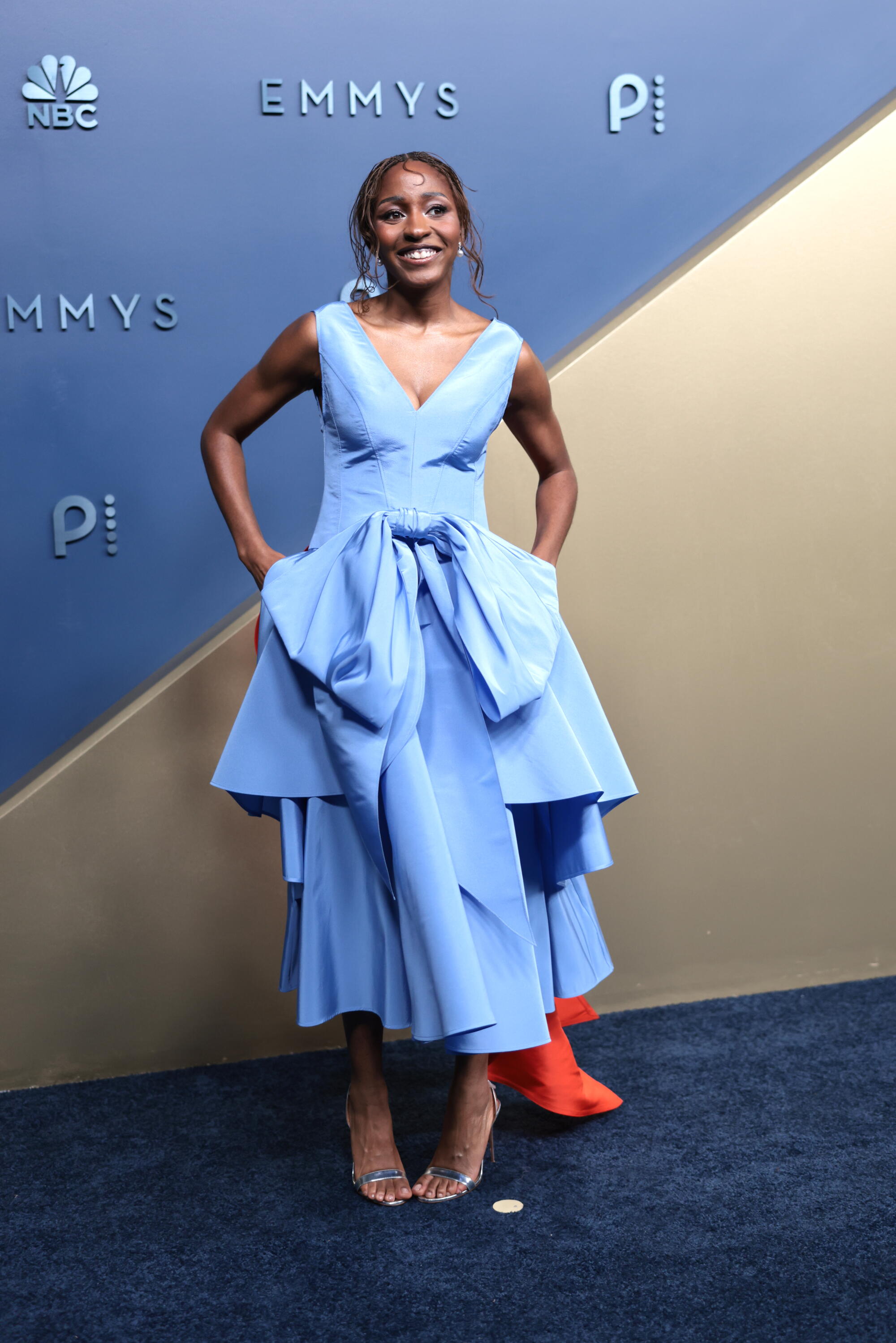 Ayo Edebiri, wearing a tiered blue gown, poses on the Emmys blue carpet. 