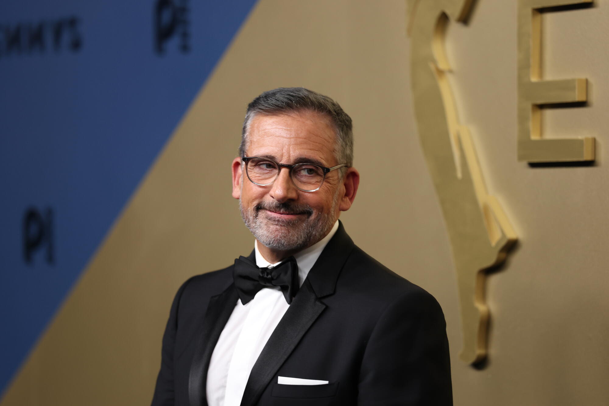 Steve Carell, wearing a tux, poses on the Emmys blue carpet.  