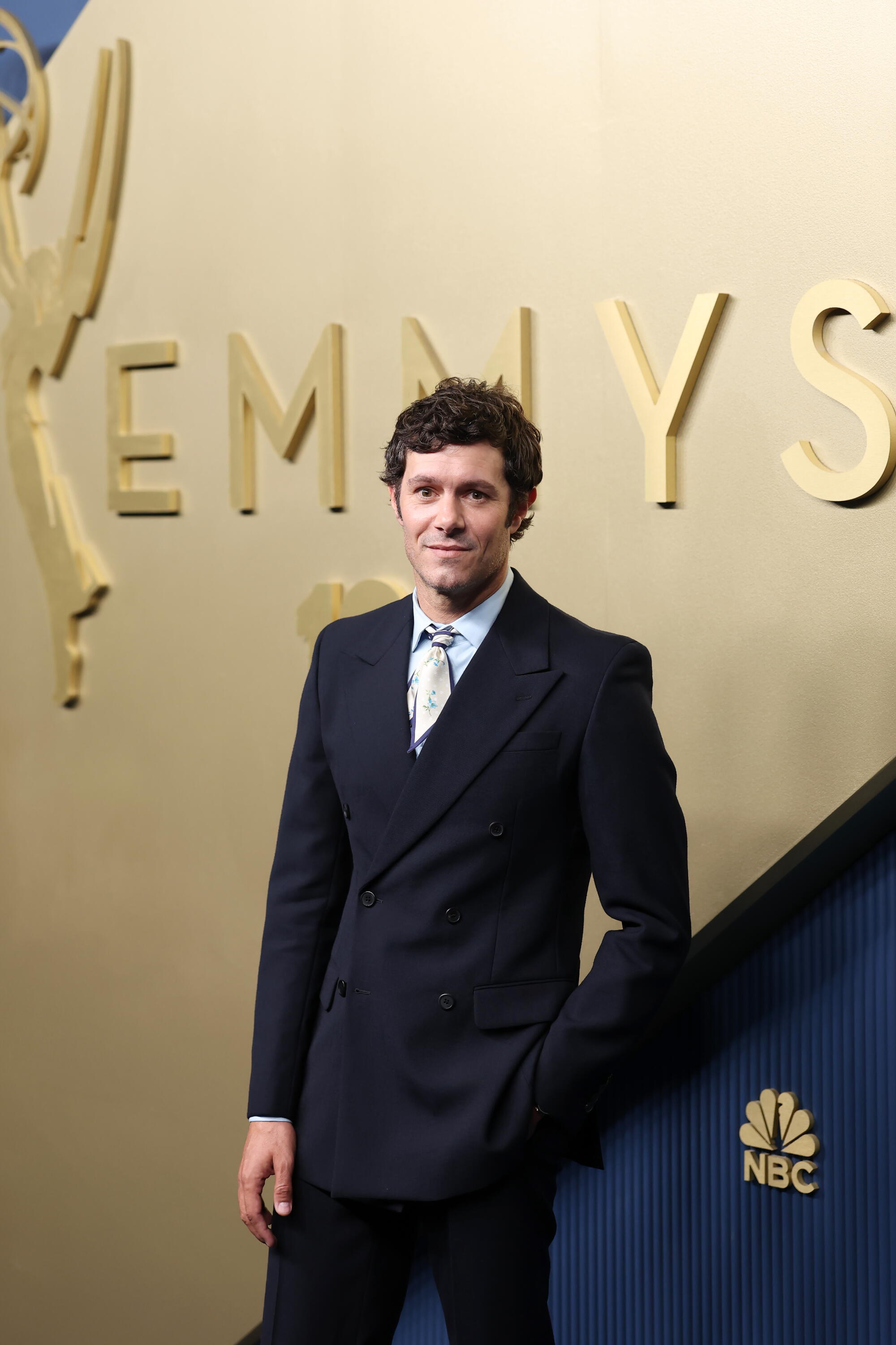 Adam Brody, wearing an oversized suit, poses on the Emmys blue carpet. 