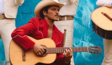 Photo of Bruno Mars wearing a red suit, a white hat, and holding a guitar.