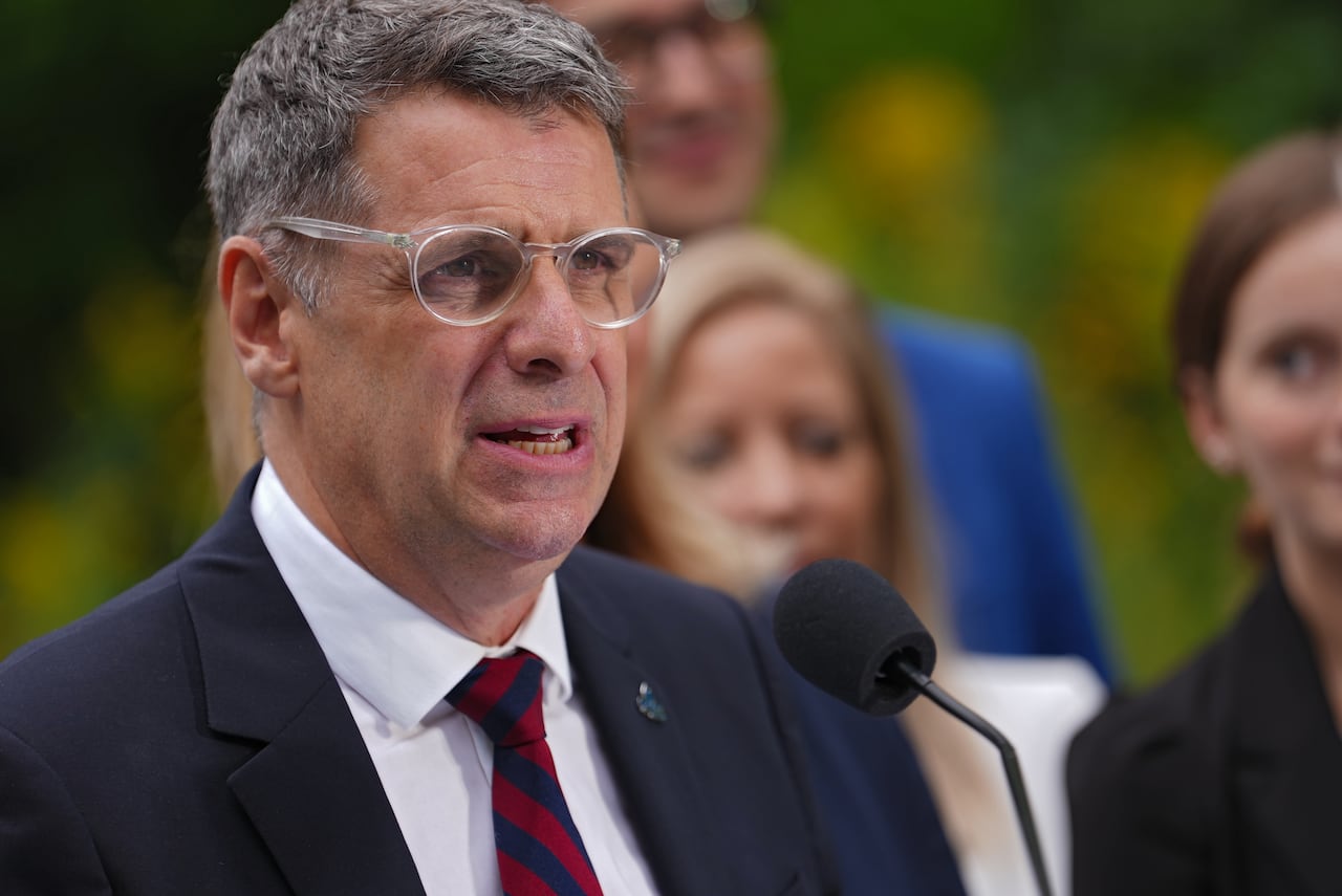 A man in a suit wearing glasses behind a microphone.
