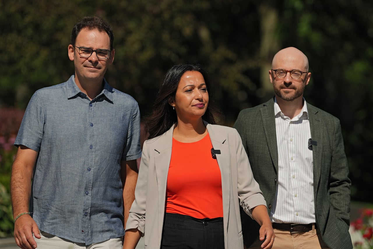 Three people walk towards the camera, the woman in the middle wears an orange shirt.