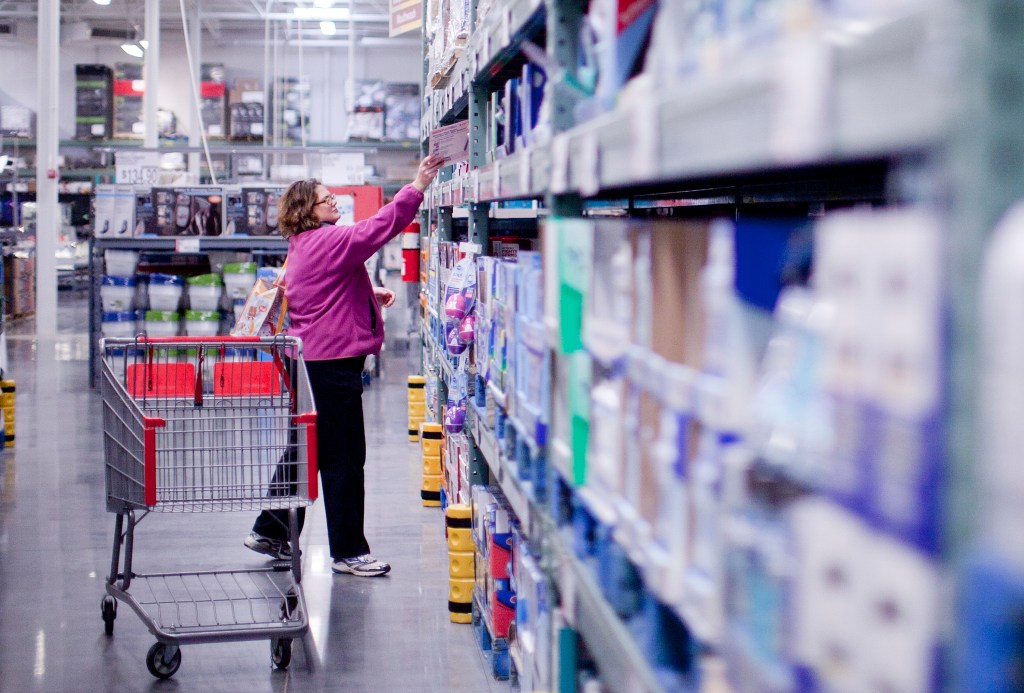 A woman shopping at a wholesale club, reaching for an item on a shelf.