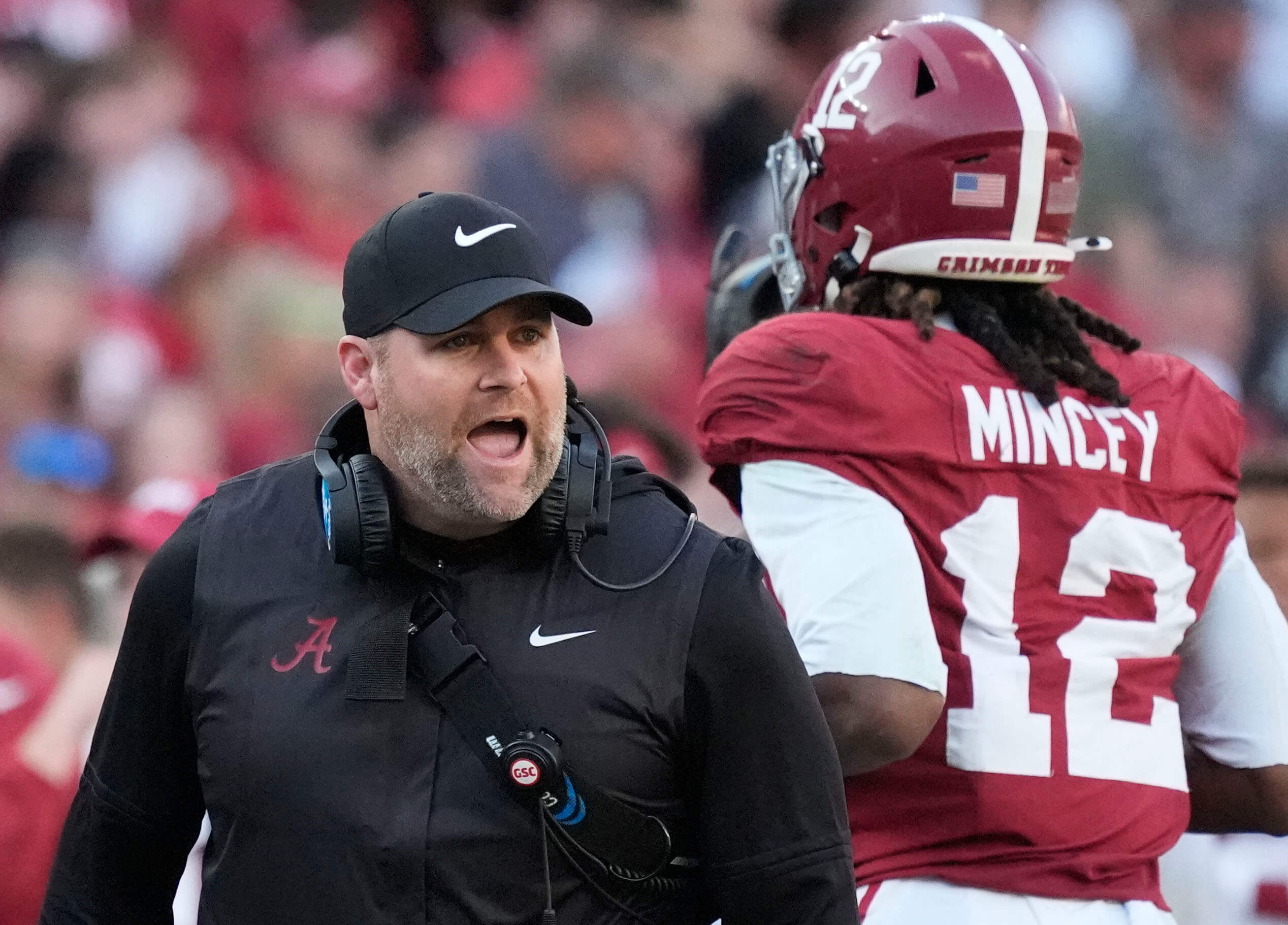 Kane Wommack calls out to a player with his headset around his neck and another Alabama player running past him