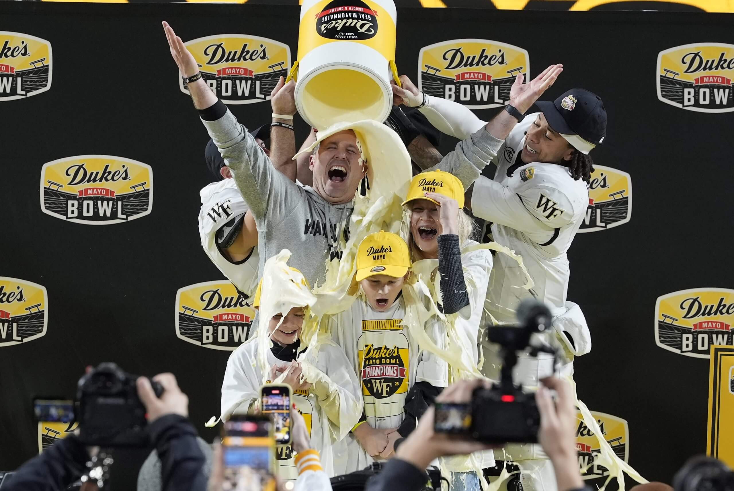 Jake Dickert raises his arms as players dump a bucket of Duke's Mayo on the heads of him and his family