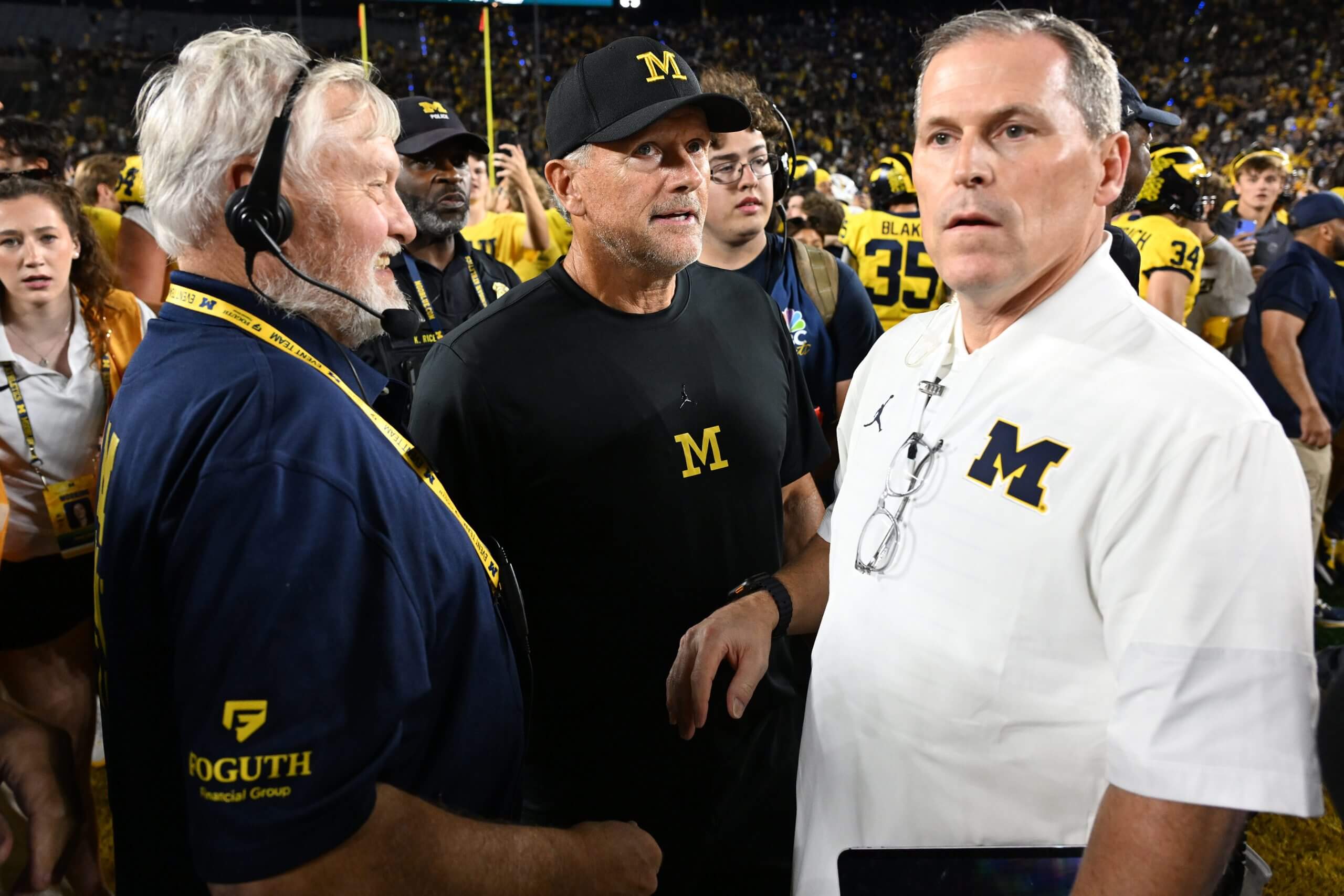 Kyle Whittingham walks off the field surrounded by fans, players and Michigan staffers