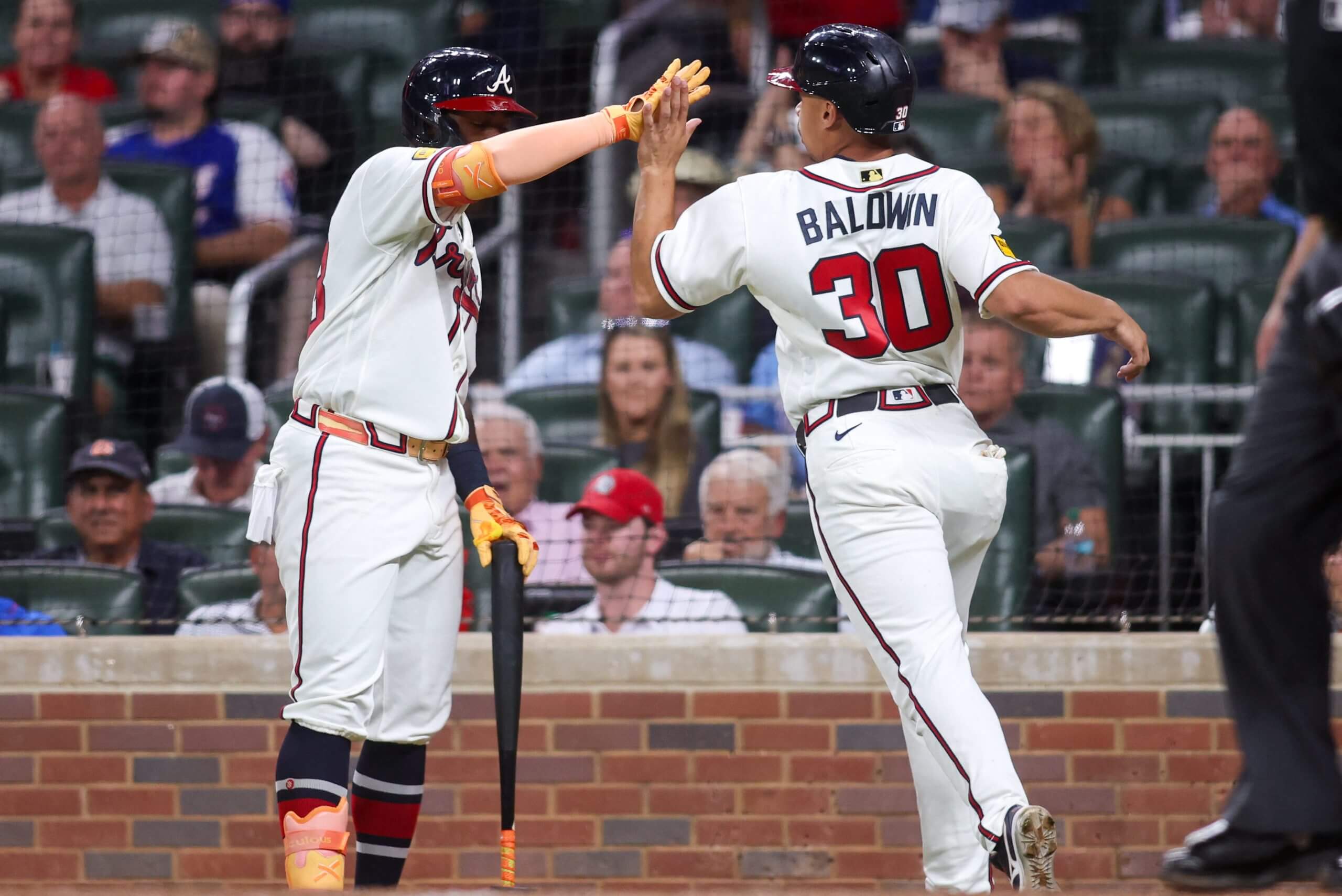 Atlanta Braves catcher Drake Baldwin, with a No. 30 on the back of his white jersey, slaps hands with teammate Michael Harris II, who has his right arm raised and extended.