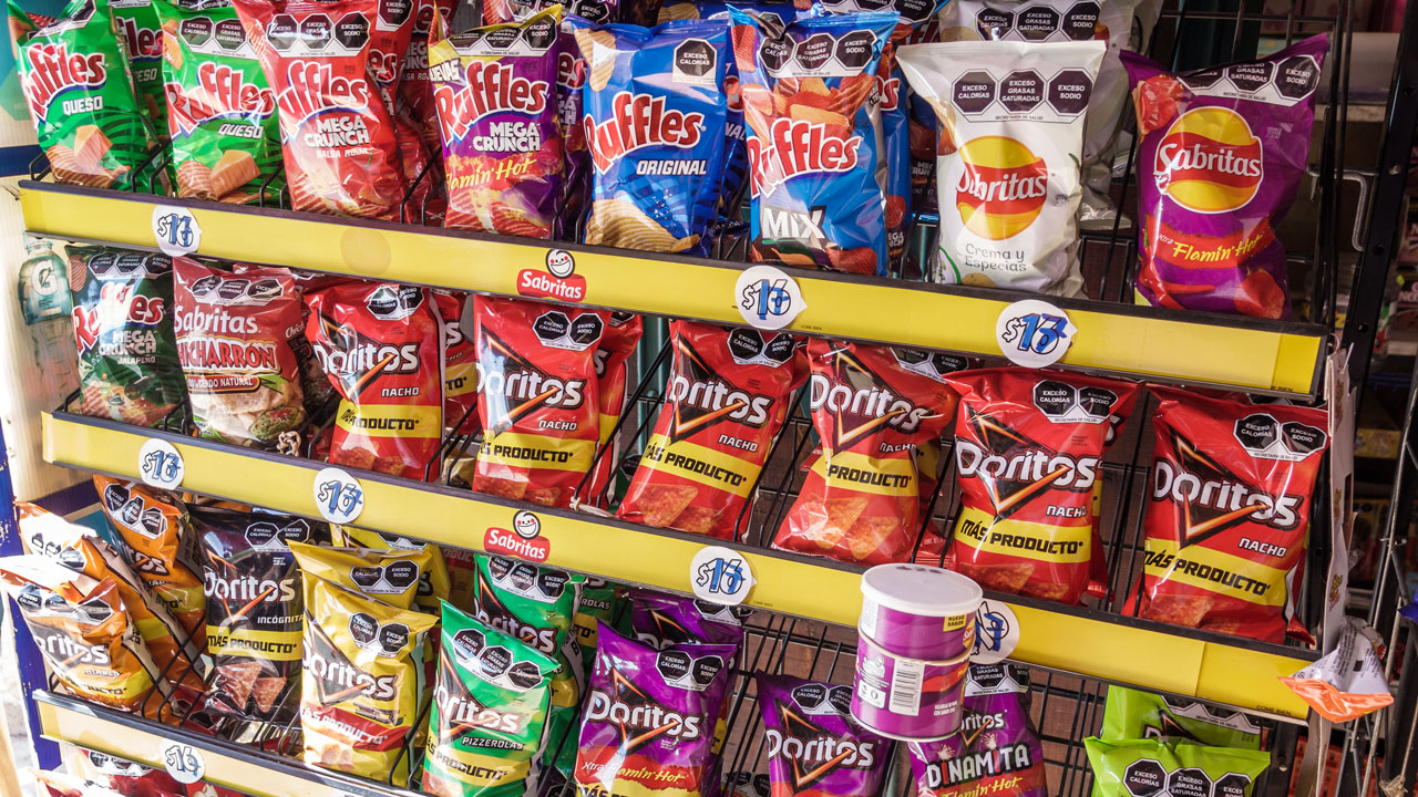 Shelves stocked with assorted bags of Mexican chips, including Ruffles, Sabritas, and Doritos, in various colorful packaging, with some Pringles cans at the bottom.
