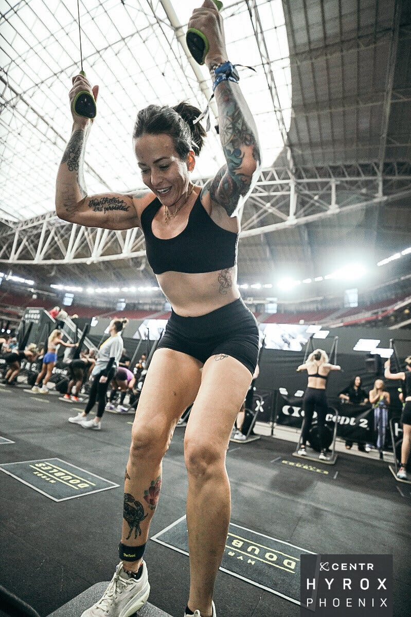 A woman with tattoos exercising energetically in a fitness competition setting.