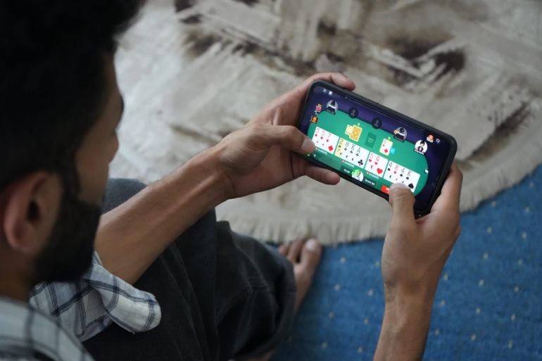 A young Indian man playing a money-based card game on his phone