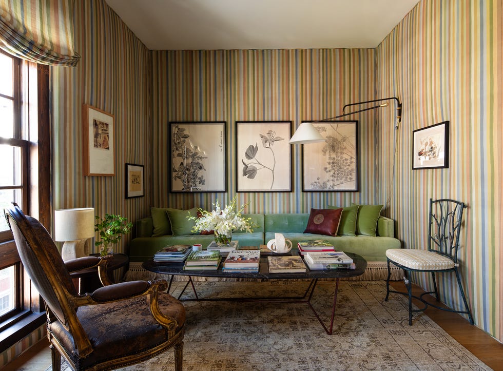Cozy living room featuring a green couch, colorful striped walls, artwork, and a glass coffee table with books.