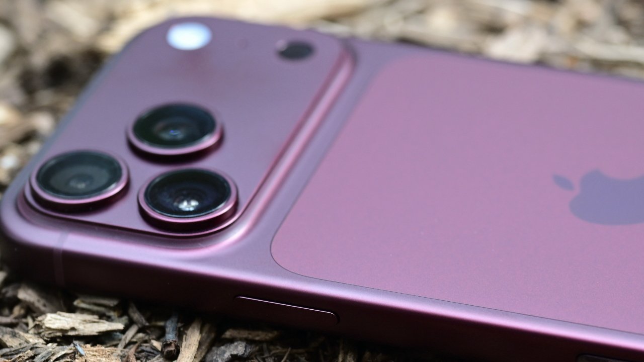 Close-up of a purple iPhone lying face down on rough wood chips, highlighting its triple rear camera lenses and sleek metallic finish