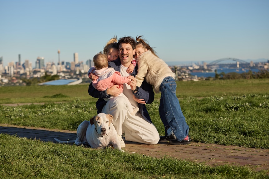 A man hugs his children with the Sydney Harbour Bridge in the background
