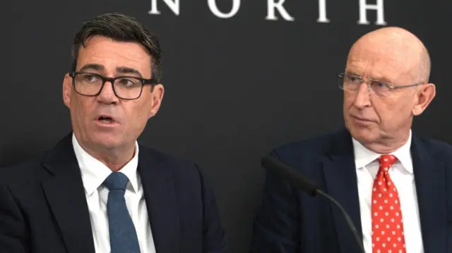 Andy Burnham and John Healey are pictured sitting together, both wearing suits and ties. There is a black background behind them with the word 'North' on it.