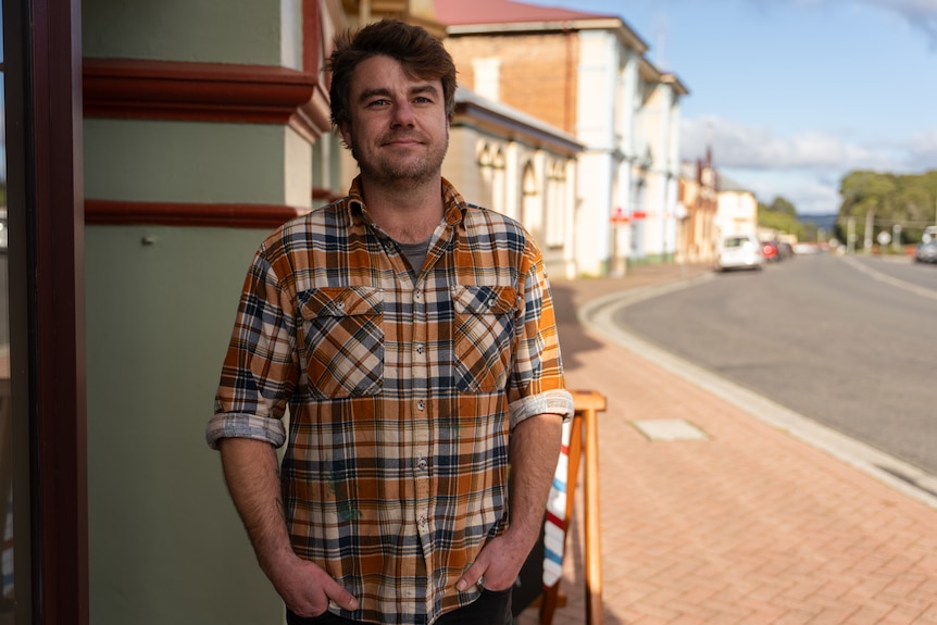 A man in a flannelette shirt poses for a portrait in a small town's main street.