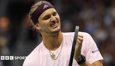 Alexander Zverev, wearing a light pink shirt and with gold jewellery around his neck, grimaces while holding his racquet during his second-round win over Quentin Halys at the US Open