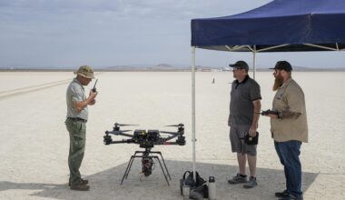 One man communicates with a hand-held radio, as two other men wait to the side for the go-ahead command to fly an experiment on a drone.