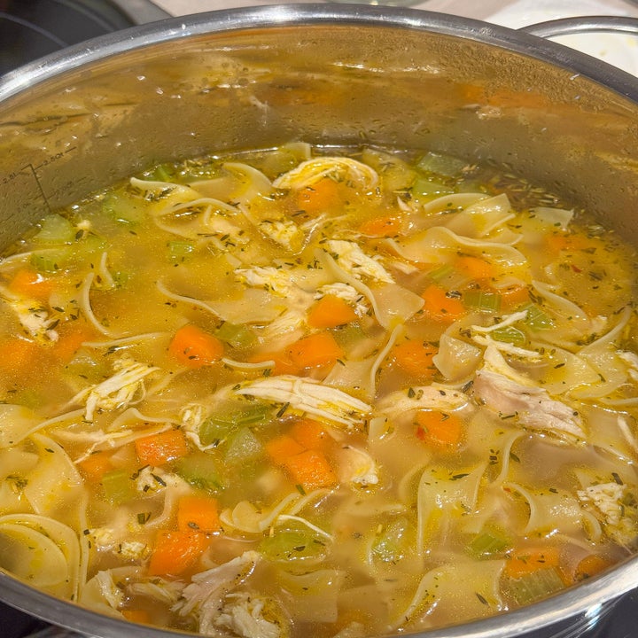 A pot of chicken noodle soup with visible chunks of chicken, carrots, celery, and noodles in broth