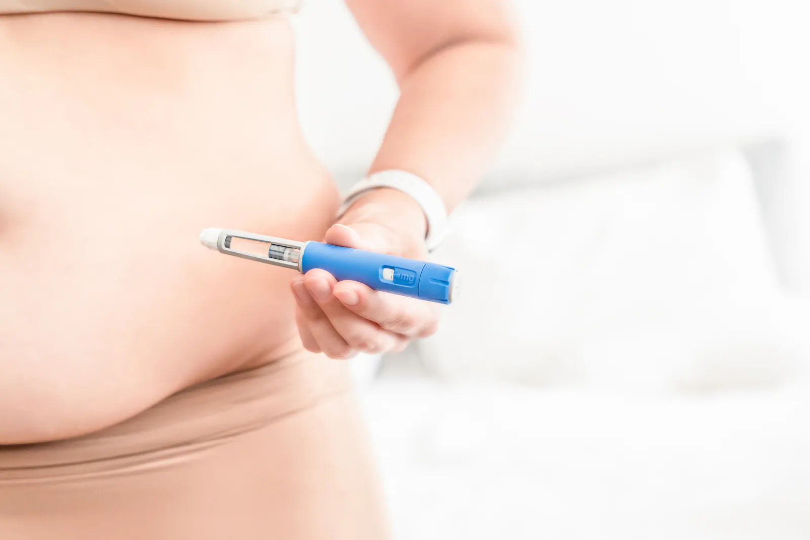 Stock image: an overweight woman holds a GLP-1 injection pen near her abdomen before self-administering medication.
