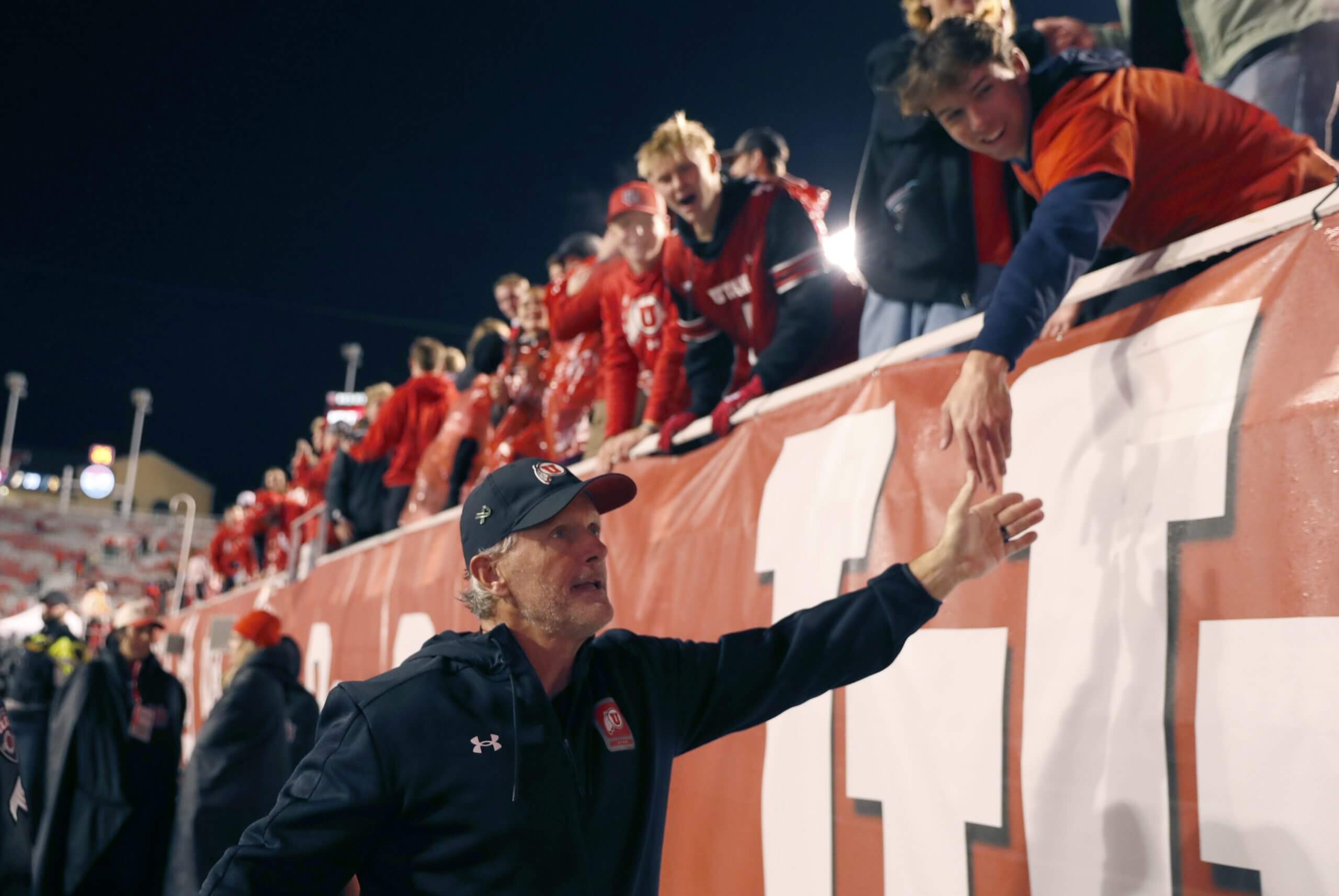 Kyle Whittingham reaches up to high-five a Utah fan while exiting the field