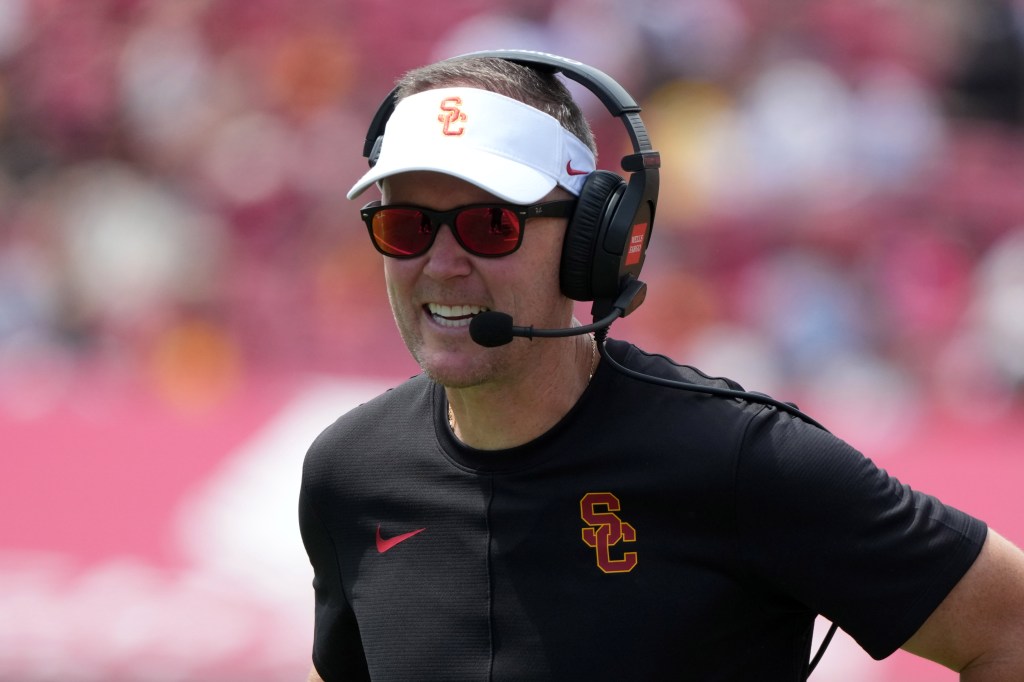 A man in a black shirt, a white visor, and sunglasses with a headset and microphone on his head.