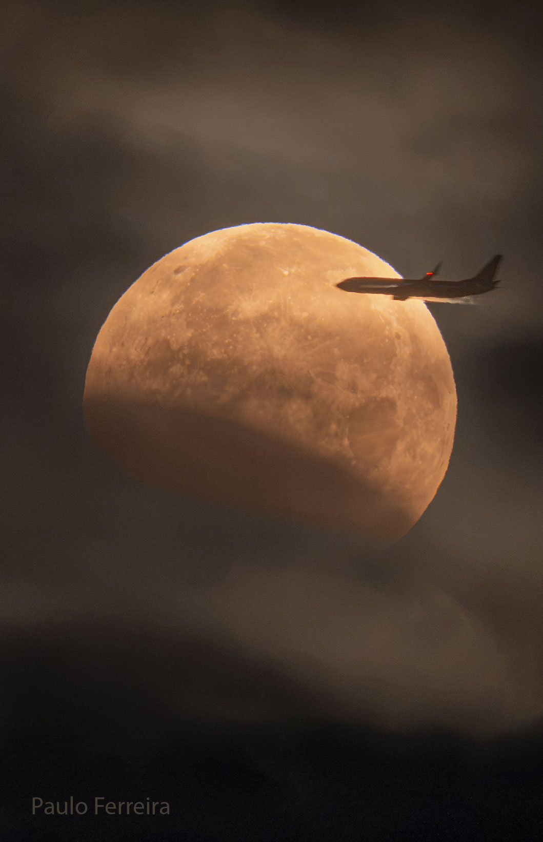 The Moon is seen in front of clouds but with part
of its lower left being unusually dark. On the upper
right, a foreground airplane appears flying into the disk of
the Moon.
Please see the explanation for more detailed information.