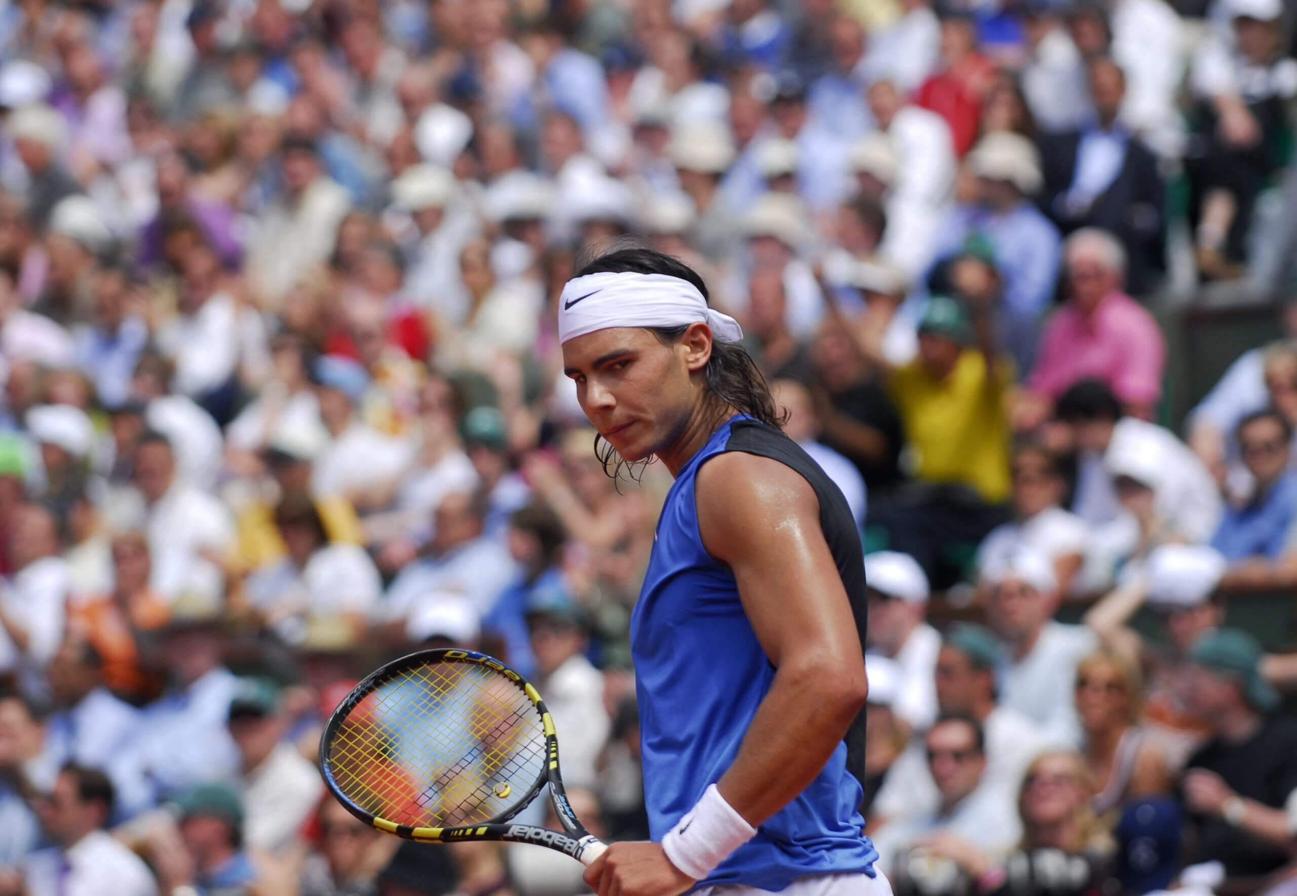 Rafael Nadal looks to his left wearing a blue tank top and white headband.