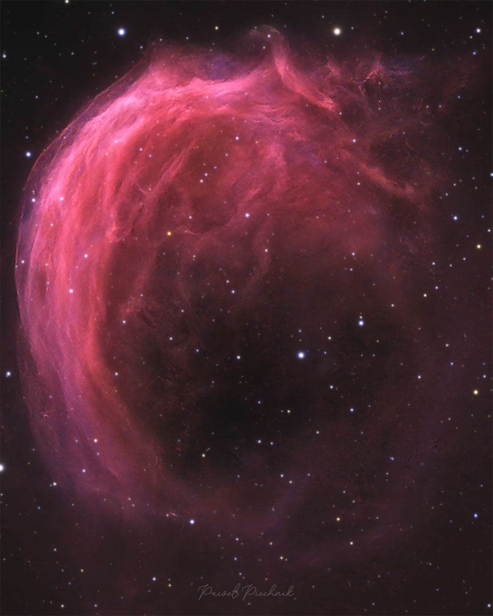 A starfield has a bright pink swirling nebula
in it. The top part of the nebula shows much detail,
while the bottom part is mostly open.
Please see the explanation for more detailed information.
