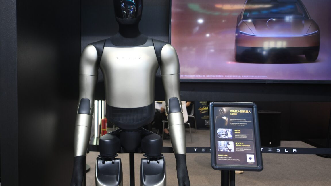 Tesla's Optimus Gen-3 humanoid robot at an exhibition in Hangzhou, Zhejiang Province, China on September 23, 2026. The robot is standing in front of a screen displaying a car.