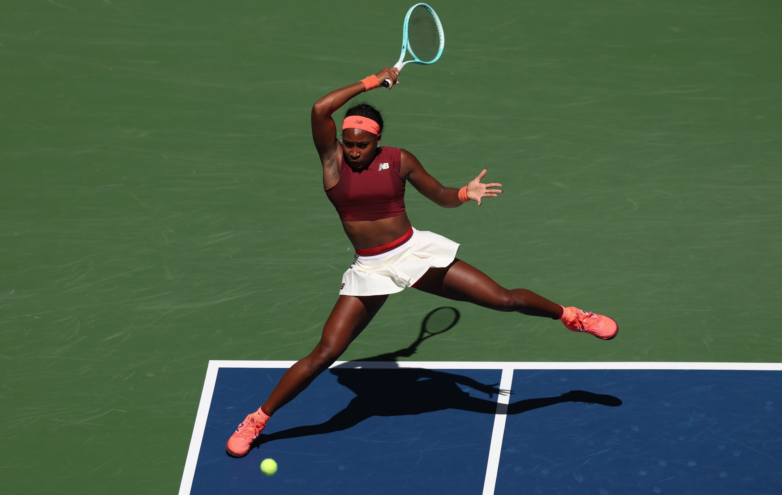 Coco Gauff hits a forehand off her right foot, with her racket high above her head.