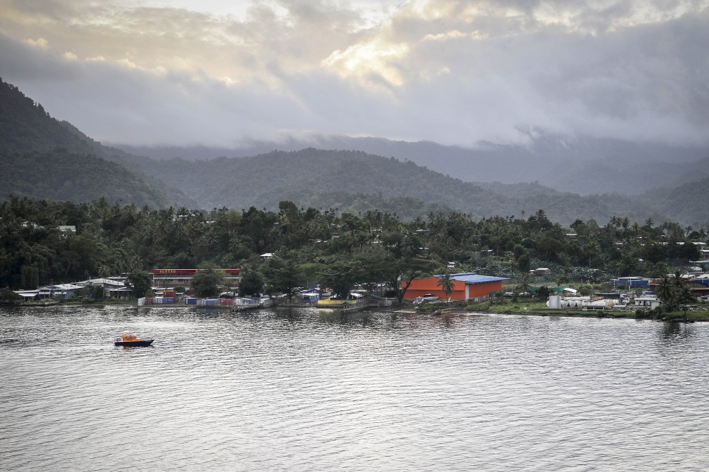 The town of Alotau in Papua New Guinea, with a small boat in the foreground and mountains in the background.