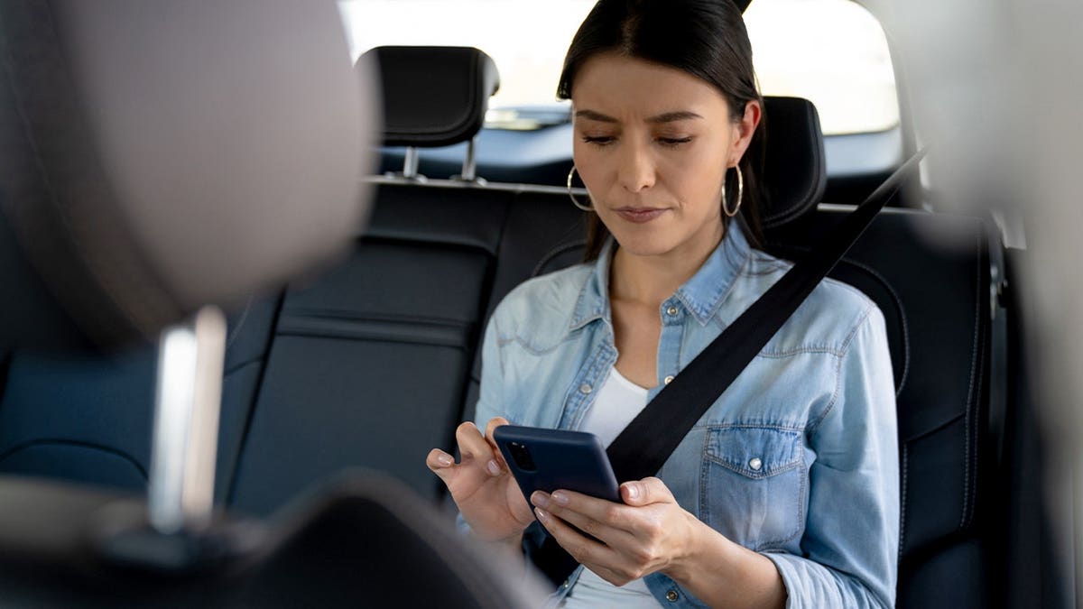 A woman uses her phone in the backseat of a car.