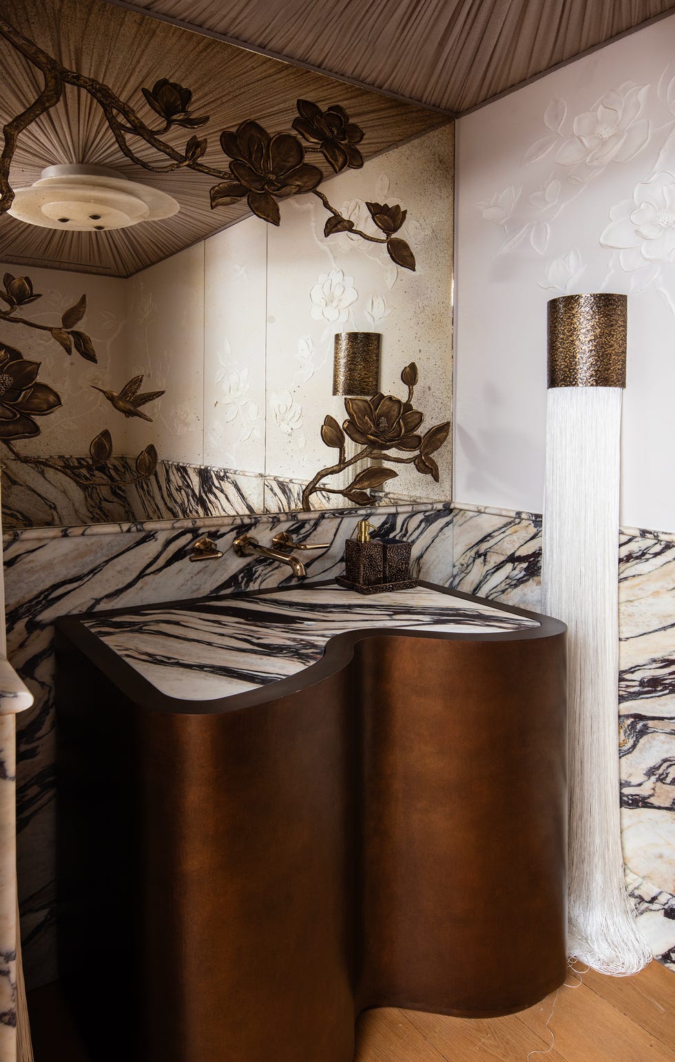 Elegant bathroom featuring a sculptural sink, marble surfaces, floral wall art, and unique lighting.