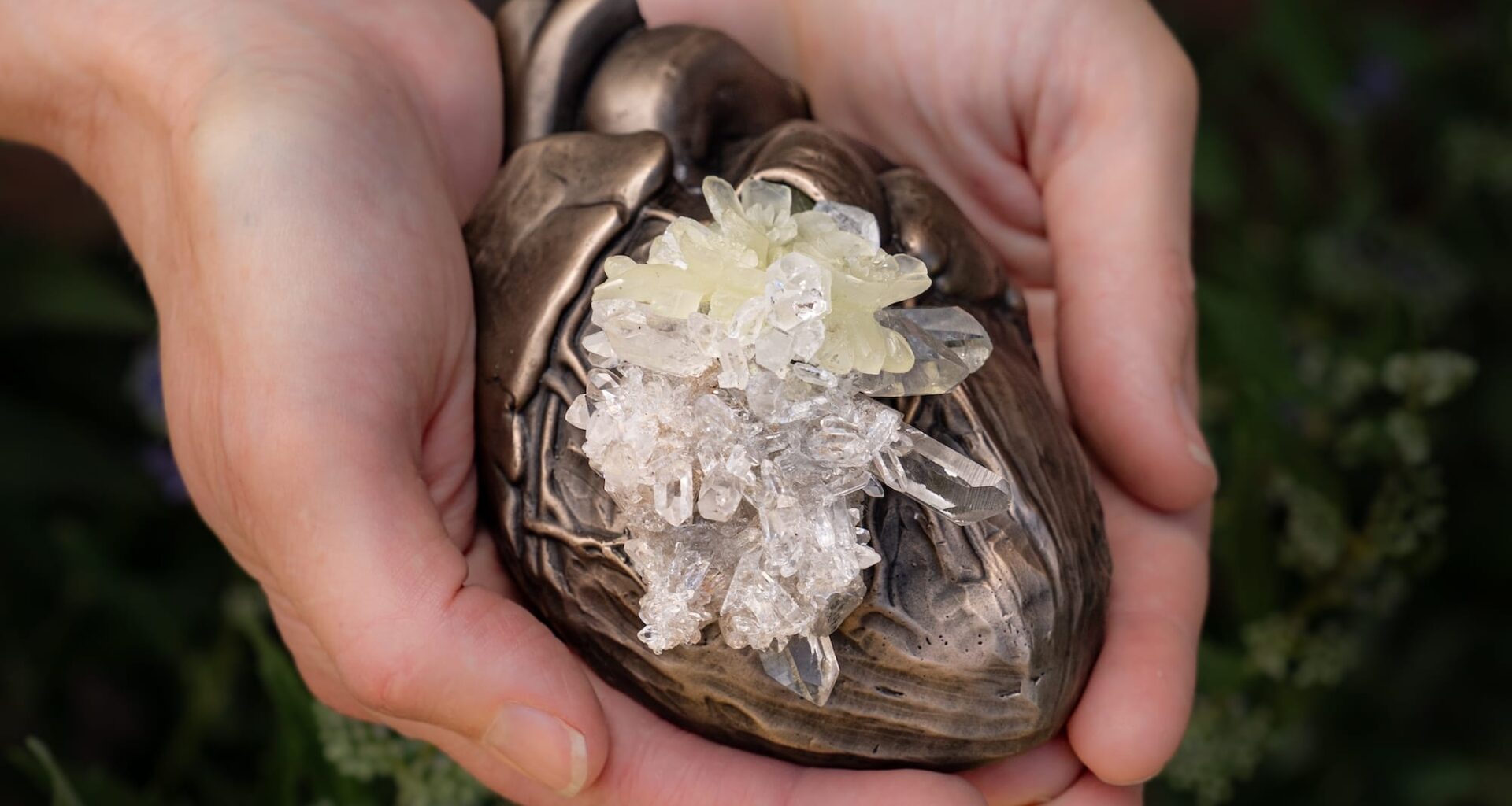 hands hold a small bronze sculpture of a human heart with crystals growing in the center of it