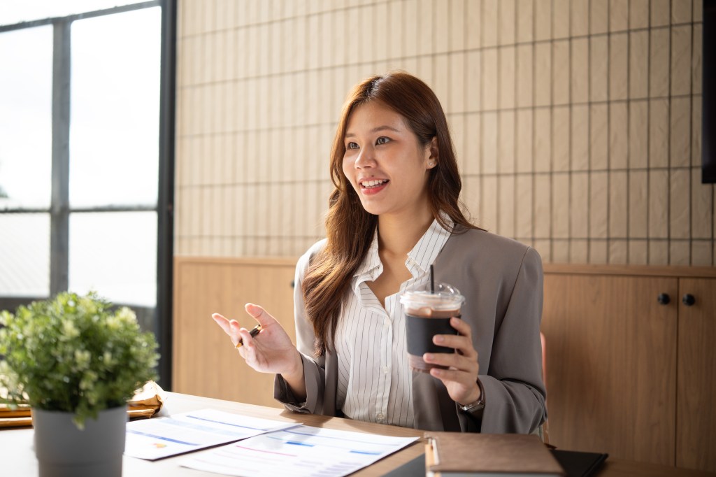 Businesswoman sitting at a desk with an iced coffee and discussing ideas.