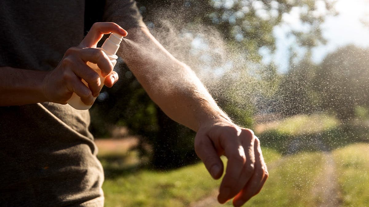 A man sprays bug spray on his arm.