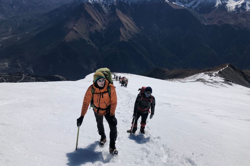 Jakob Steiner is wearing an orange top. He is hiking on a snowy mountain with someone walking behind him.