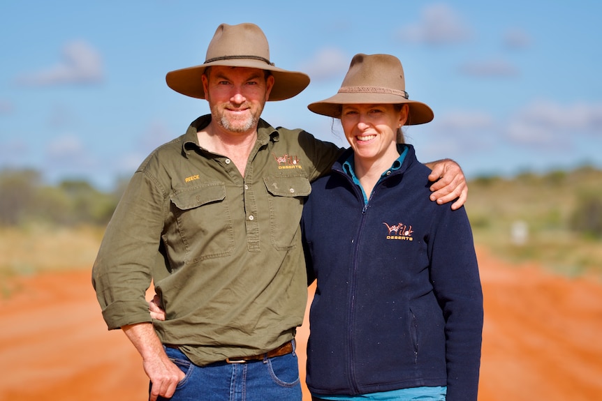 Reece Pedler and Bec West pose for a photo on the road to Cameron Corner. Both wear Akubra-style hats and collared shirts.