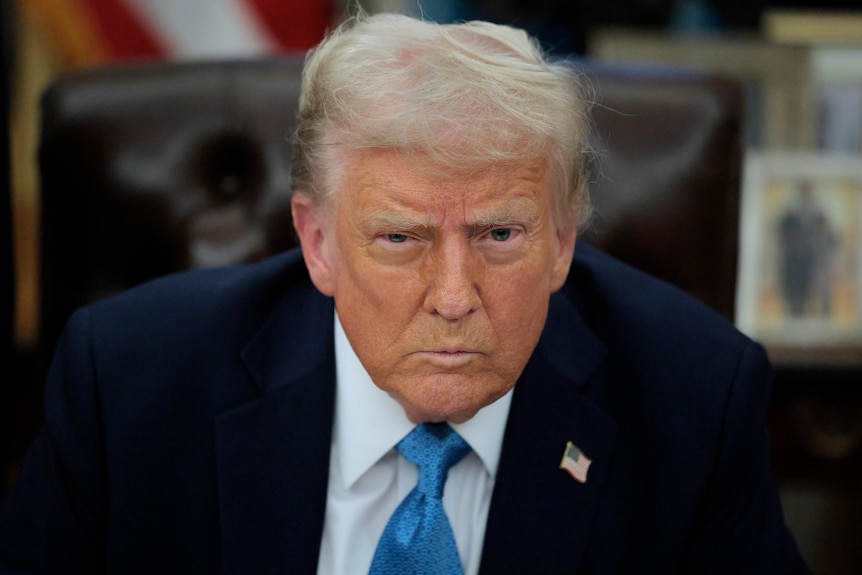 A man in a suit with pale hair stares into the camera