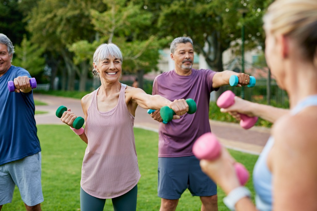 Four active senior adults lifting dumbbells outdoors in a park.