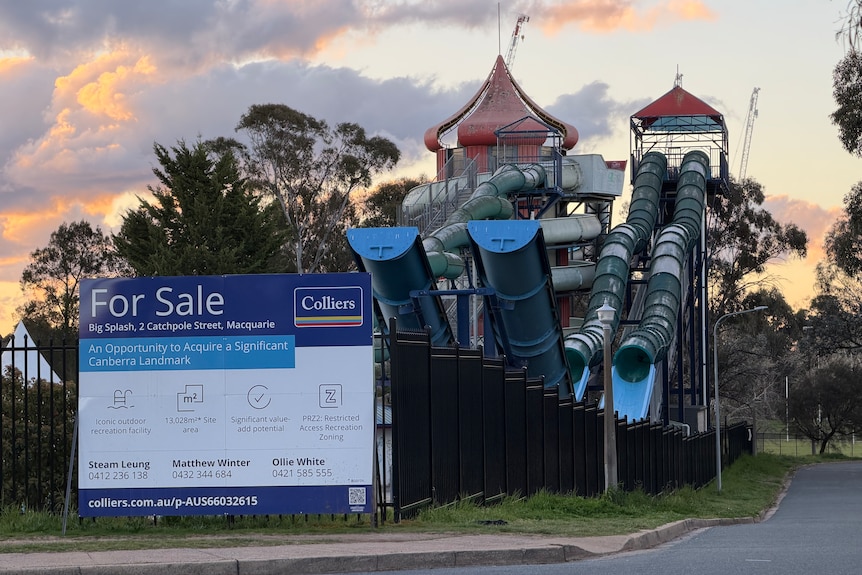 An unused water park pictured at dusk, with an empty swimming pool covered in graffiti.