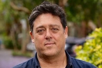 a man in a blue shirt posing in front of green plants