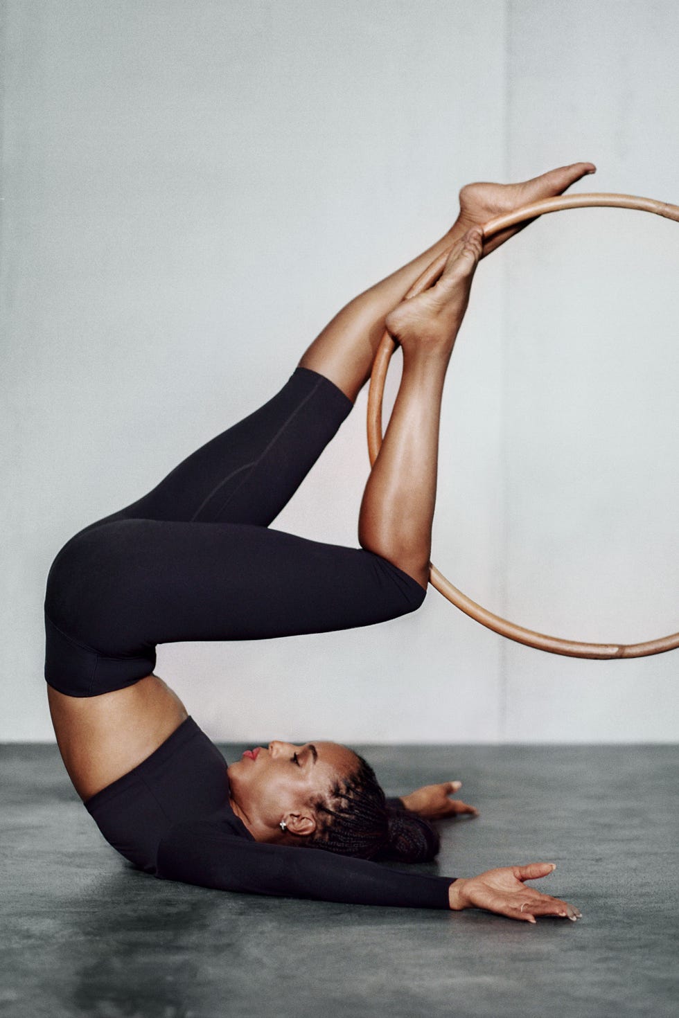 A person performing an acrobatic move with their legs in a hoop while lying on a floor.
