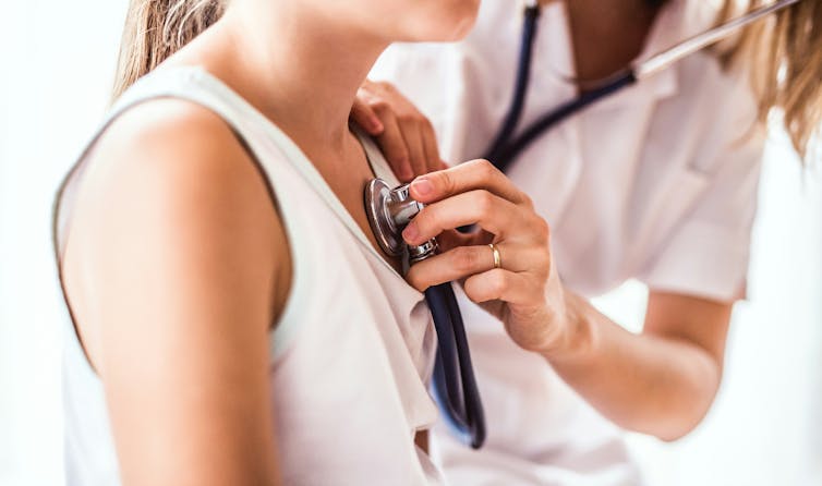 A health-care provider using a stethoscope on a young woman; both of their faces are out of frame