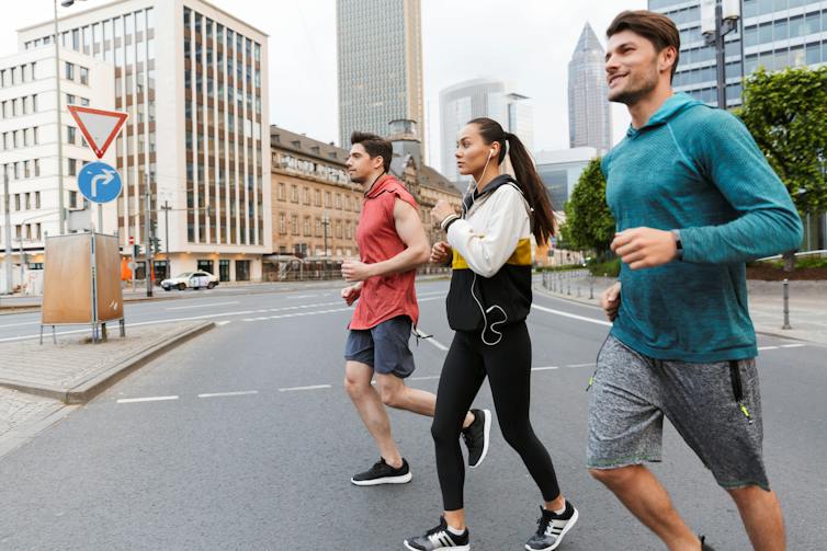 Two men and one woman go for a slow jog through a city.