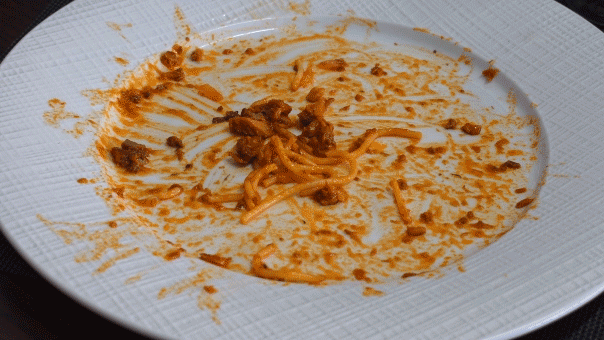 A diner places a knife and fork on a plate of nearly finished spaghetti.