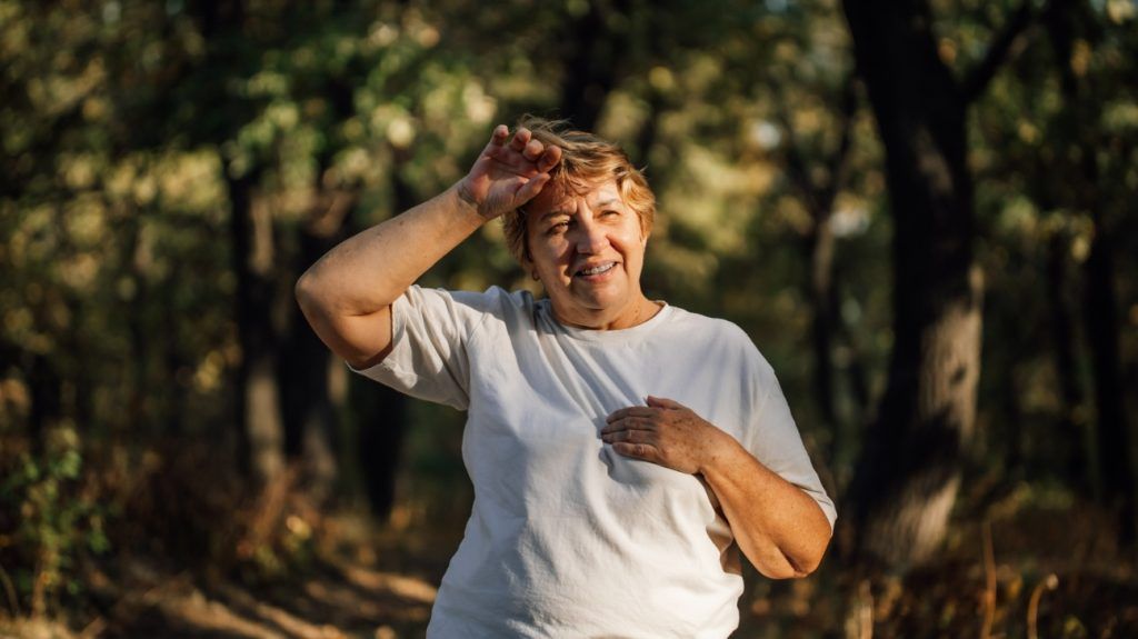 A middle-aged female adult looks tired and out of breath after walking at a brisk pace in nature among trees