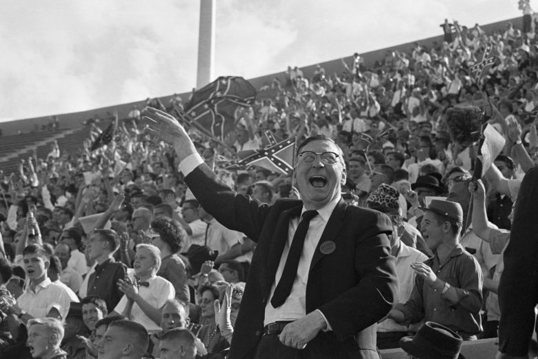 Confederate flags wave behind then Mississippi Governor Ross Barnett as he yells along with the rest of the crowd as the Rebels defeat Houston University, in Jackson, Mississippi.